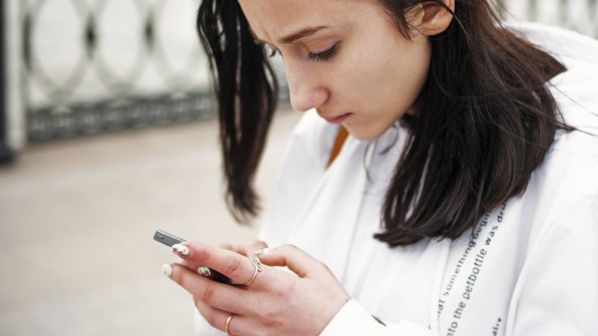 O tânără cu un hanorac alb tine un telefon in mana si citeste ceva atenta