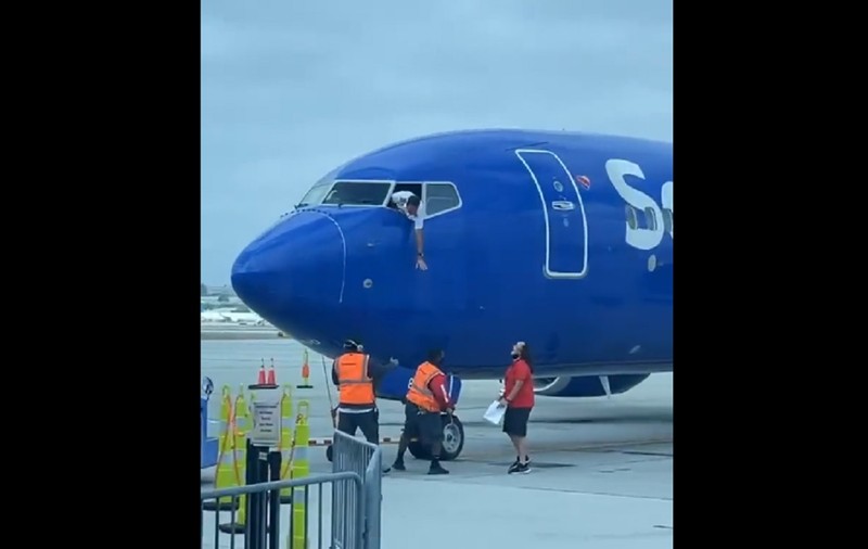 Pilotul unui avion atârnă pe fereastra cabinei, ca să ia telefonul uitat în aeroport de un pasager care era deja îmbarcat