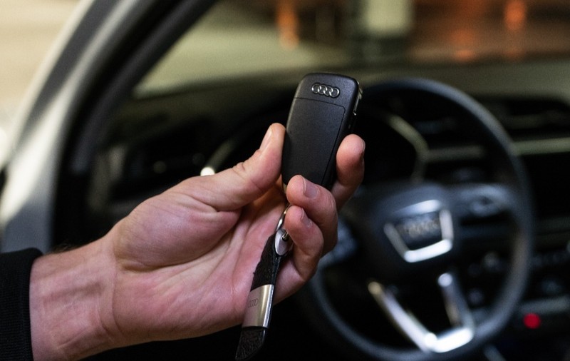 Un bărbat care ține cheile unui AUDI, care se vede în fundal