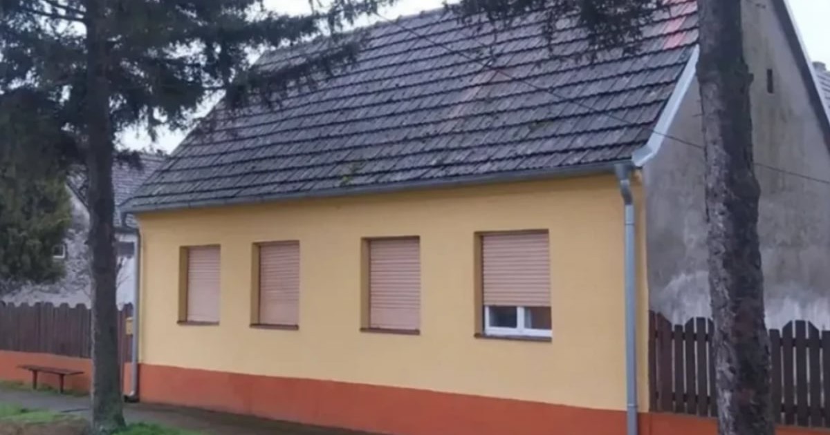 Casă cu fațadă vopsită în galben și portocaliu, patru ferestre și un acoperiș din țiglă.