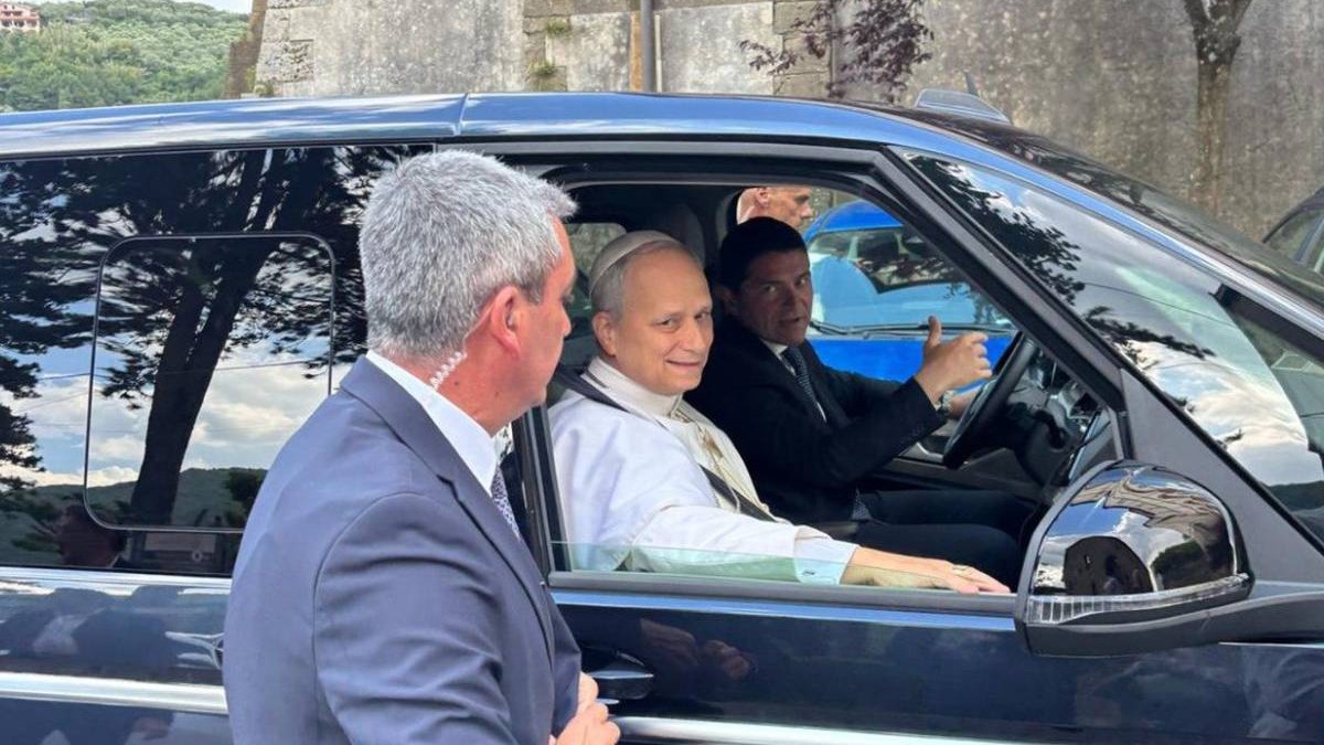 Papa Leon al XIV-lea așezat pe locul din dreapta-față al unei mașini Volkswagen Multivan, în timp ce este escortat de un șofer și personal de securitate.