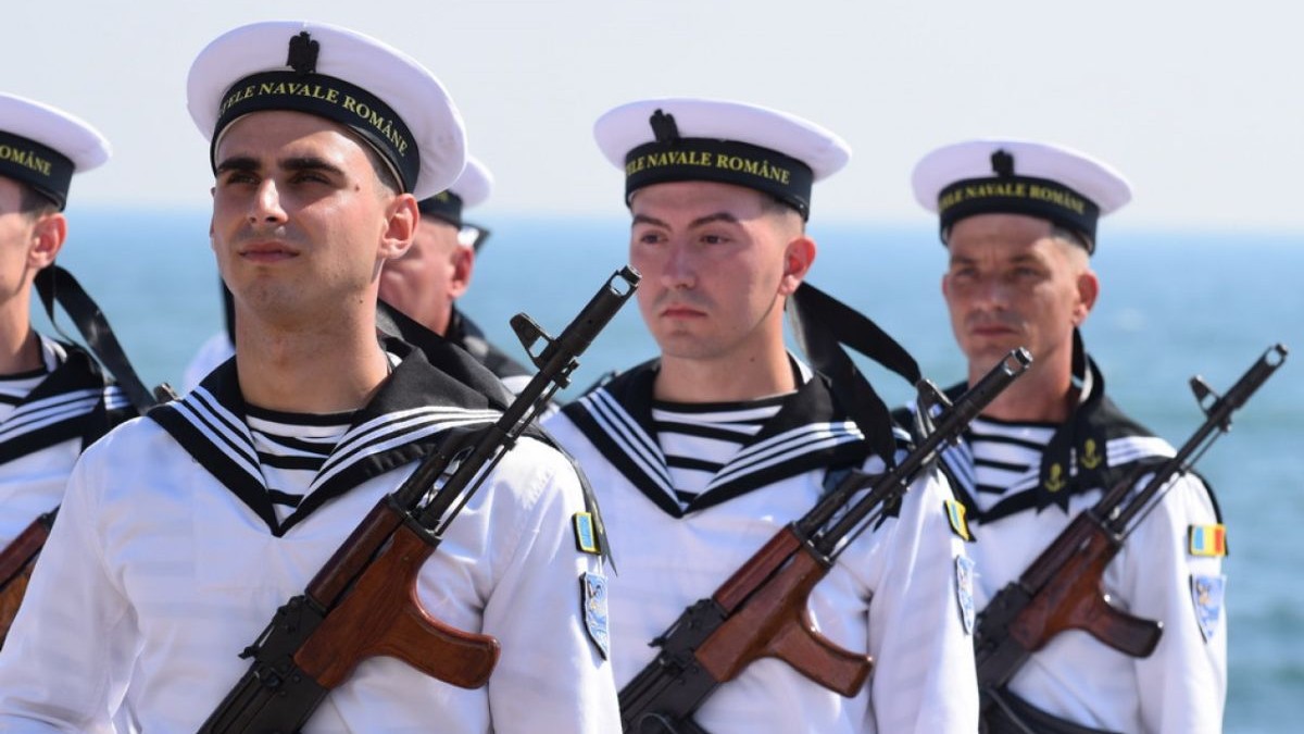 Militari din Forțele Navale Române, îmbrăcați în uniforme albe cu armele la piept, cu marea pe fundal, la Ziua Marinei 2025