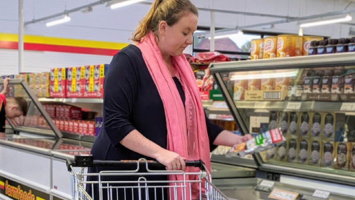 Clientă într-un supermarket Farmfoods, cu o cutie în mână, lângă coșul de cumpărături