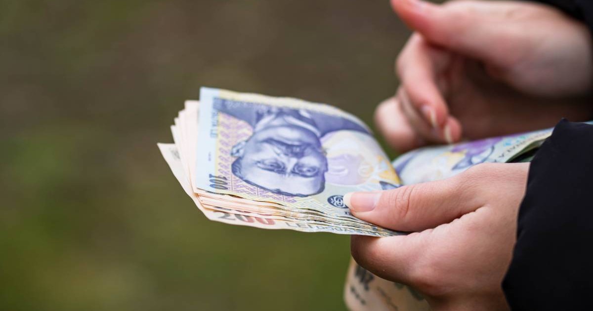 O femeie româncă care numără mai multe hârtii de 100 de lei, îi ține în mână