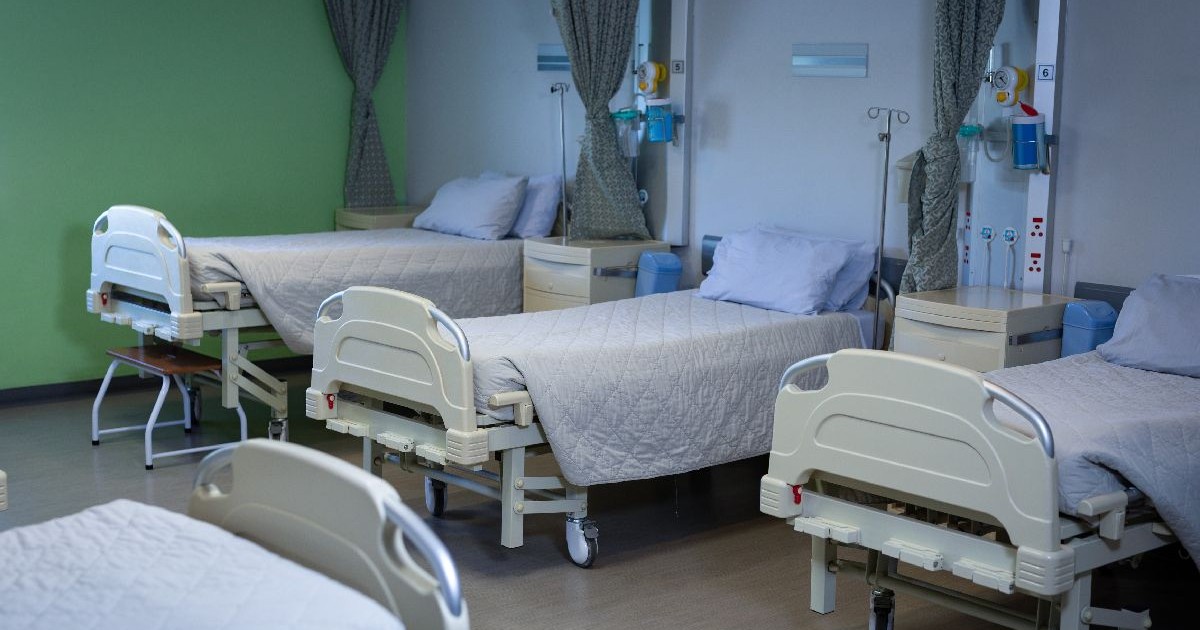 trei paturi de spital acoperite cu pături albe, într-un salon
