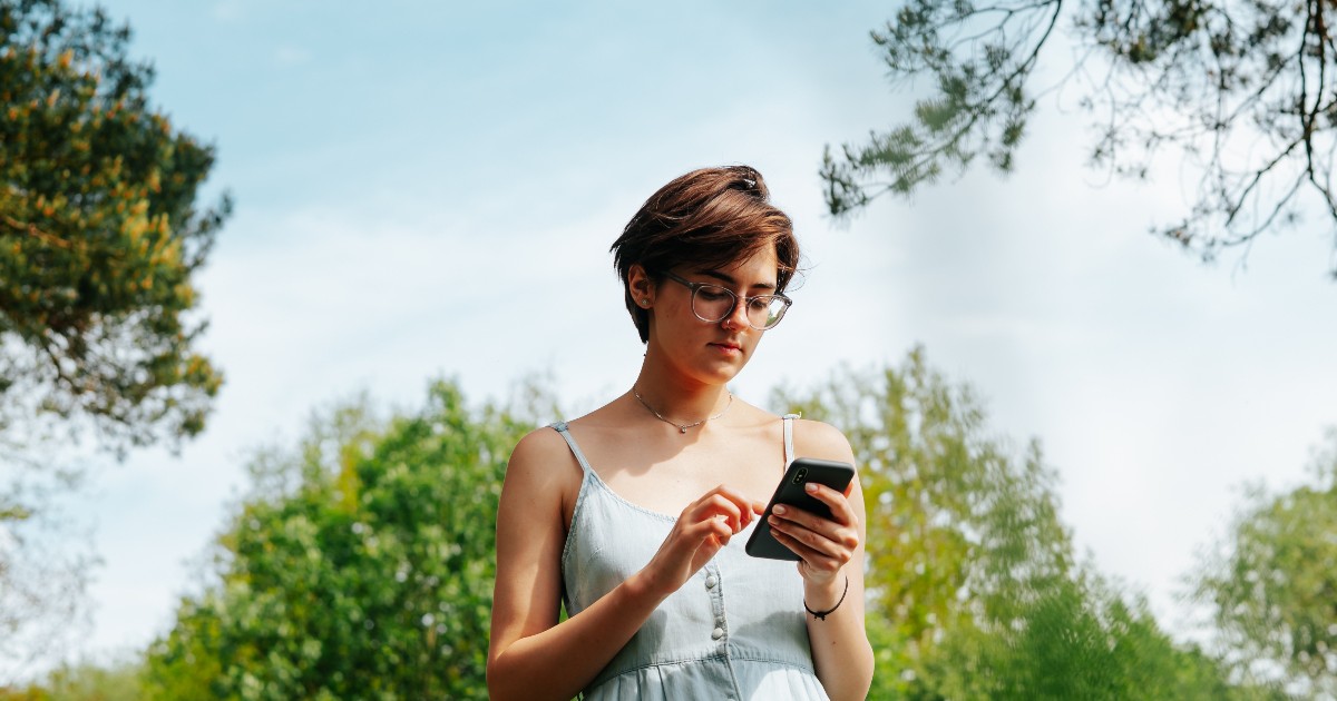 O femeie care ține un telefon în mână, poartă o rochie albastră și tastează un mesaj
