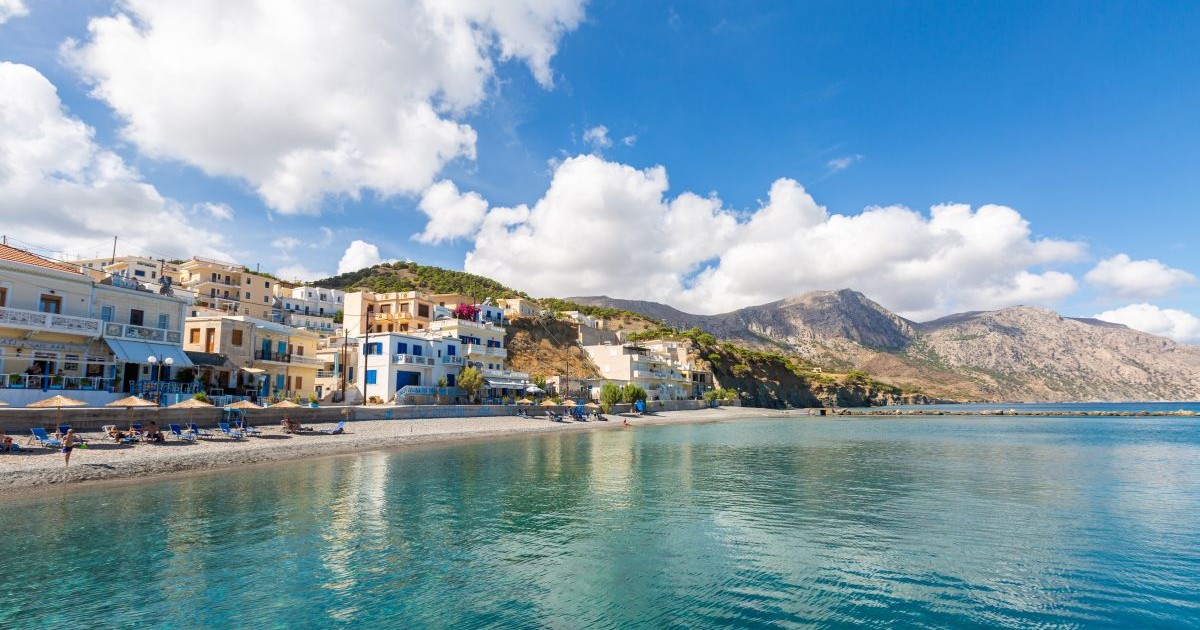 A landscape of a sea surrounded by mountains buildings and beaches under a blue cloudy sky in Greece