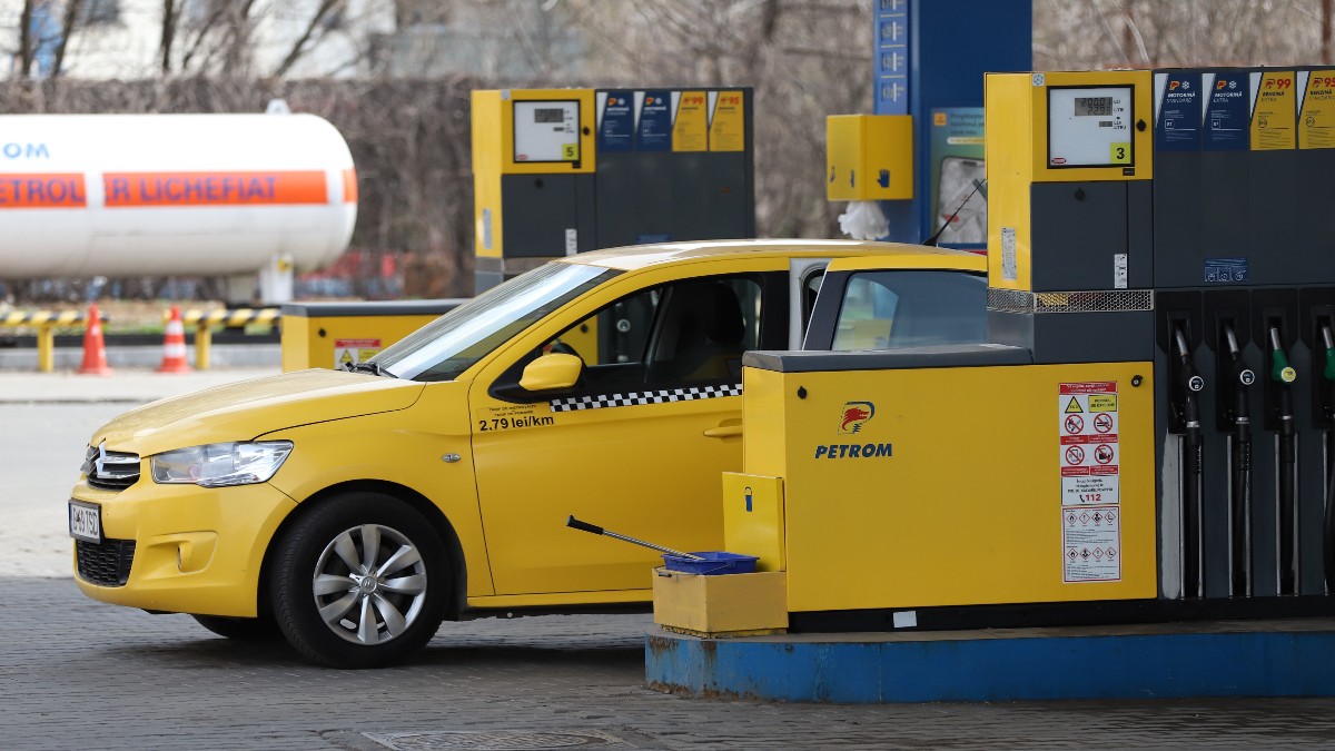 Imaginea prezintă un autoturism taxi galben staționat lângă o pompă de alimentare într-o benzinărie Petrom.