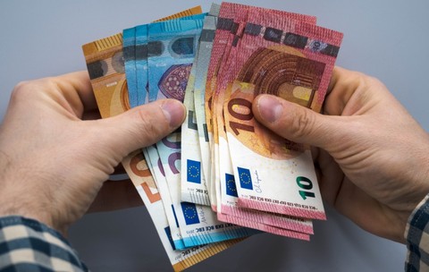 O persoană care ține bancnote de euro în mână
