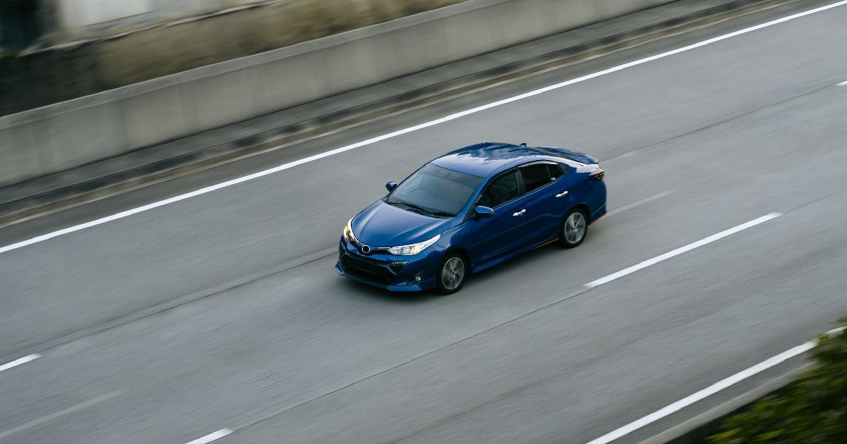 O fotografie cu un sedan albastru elegant care accelerează pe o autostradă cu mai multe benzi pe sensul de mers.