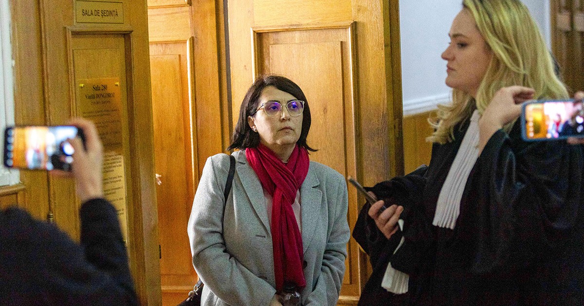 Laura Dronca cu un fular grena la gât și un pardesiu gri iese din sala de judecată fiind însoțită de avocata ei.