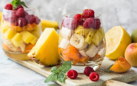 Fructe exotice și tropicale care îți dau energie: beneficii pentru sănătate și rețete - Salată de fructe cu banane, ananas și zmeură în pahare de sticlă pe un tocător de lemn