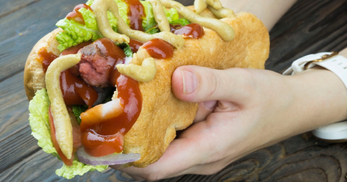 O femeie ține în mâini un hot dog care are adăugat ketchup și muștar