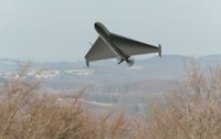 O dronă militară gri în formă de aripă triunghiulară zboară la joasă altitudine deasupra unei zone împădurite și a unui peisaj deluros. Poză cu caracter ilustrativ. Foto: Shutterstock