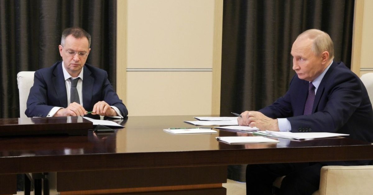 Vladimir Medinsky, stanga, și Vladimir Putin, dreapta, stau la o masa din lemn, cu acte in față