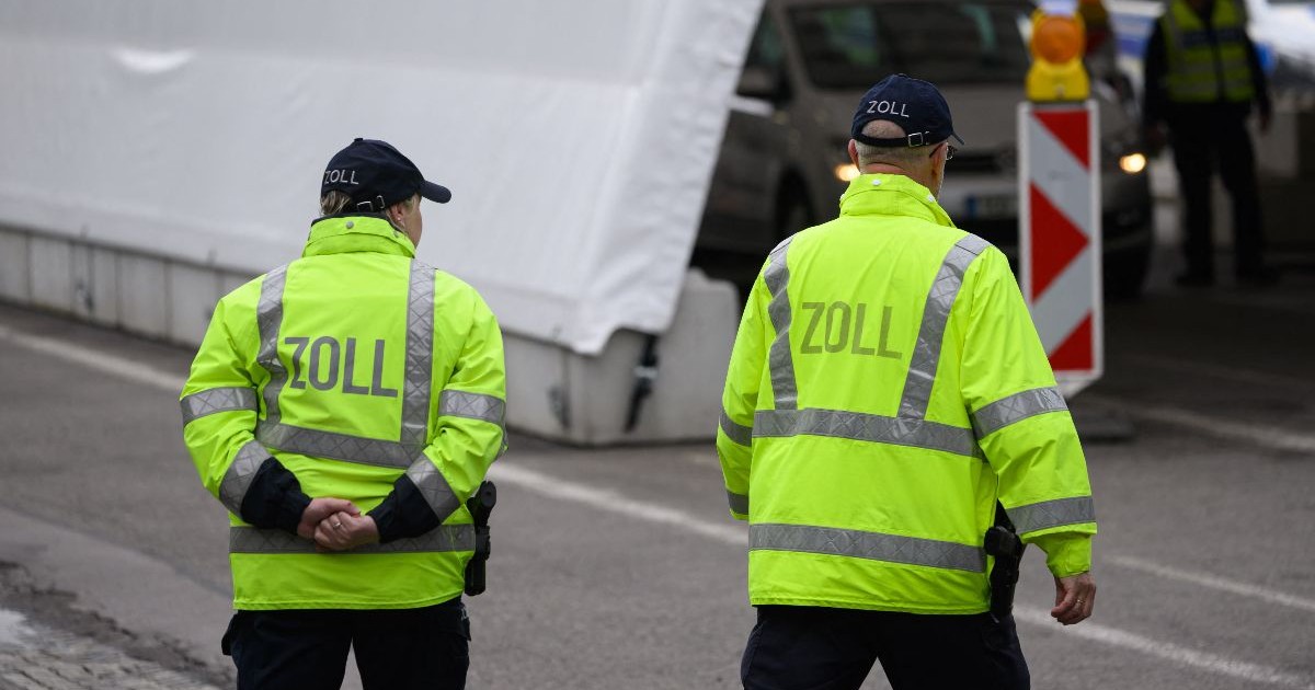 Doi polițiști îmbrăcați în jachete galbene neon stau pe stradă lângă un cort alb, în apropierea unor mașini parcate.