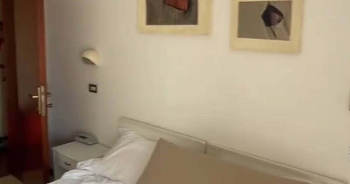 Imagine cu patul și tablourile din camera de hotel unde a fost cazată Românca. Lenjeria de pe pat este albă, în timp ce una dintre perne este crem