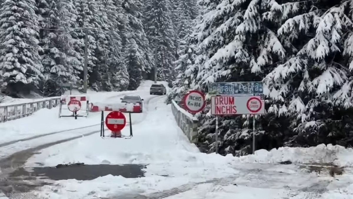 Două mașini care merg pe un drum plin de zăpadă, prinre copacii acoperiți de un strat gros de zăpadă, pe Transfăgărășan după indicatorul pe care scrie „Drum închis”