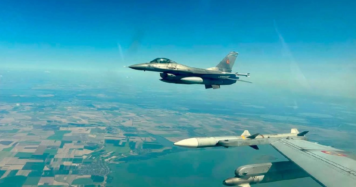 Un Avion F 16 fotografiată dintr-o altă aeronavă, căreia i se vede aripa și rachetele