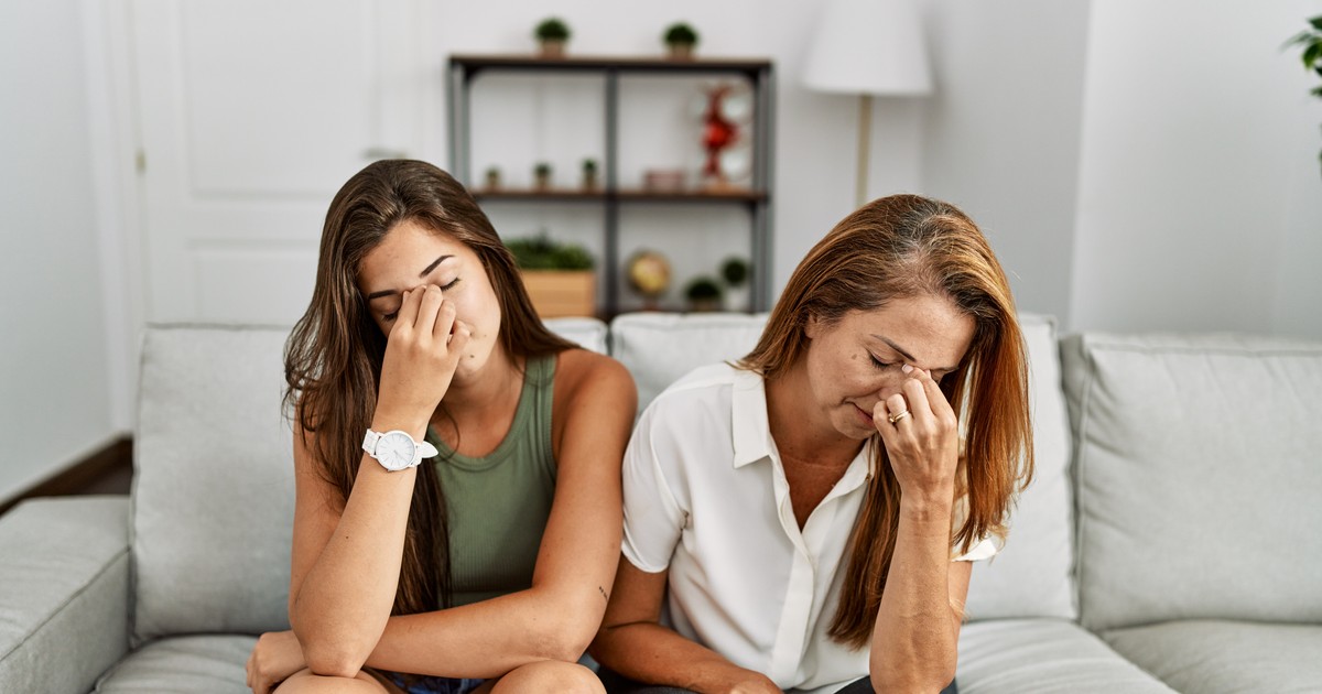 Mama și fiica stau împreună pe canapeaua de acasă, obosite, frecându-și nasul și ochii
