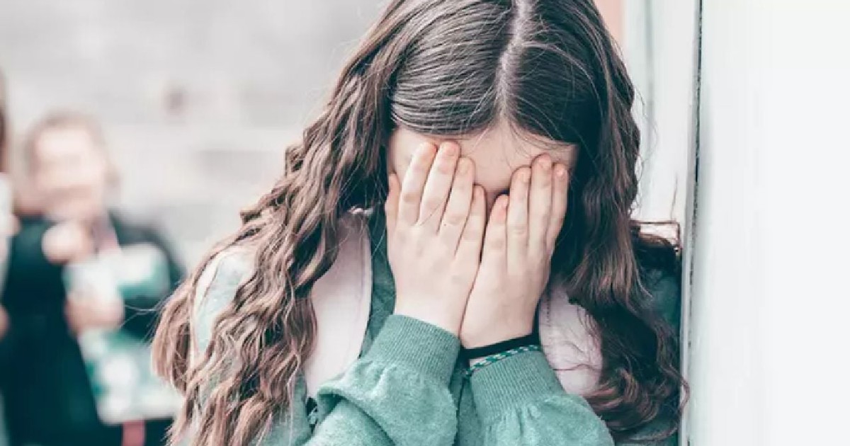 O fată minoră cu părul lung își ține mâinile în jurul ochilor