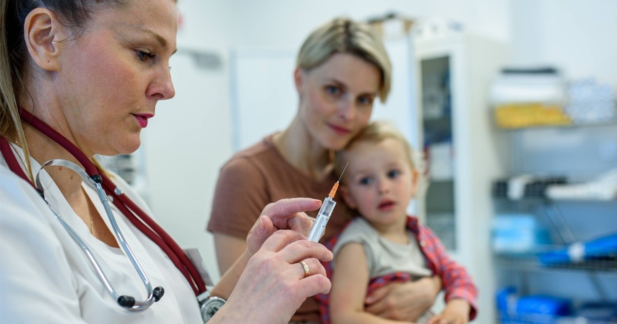 Un medic, femeie cu o seringa in mana, in cabinet, vrea sa vaccineze un copil. Vaccinare scazuta rujeola epidemie. Foto: Imago