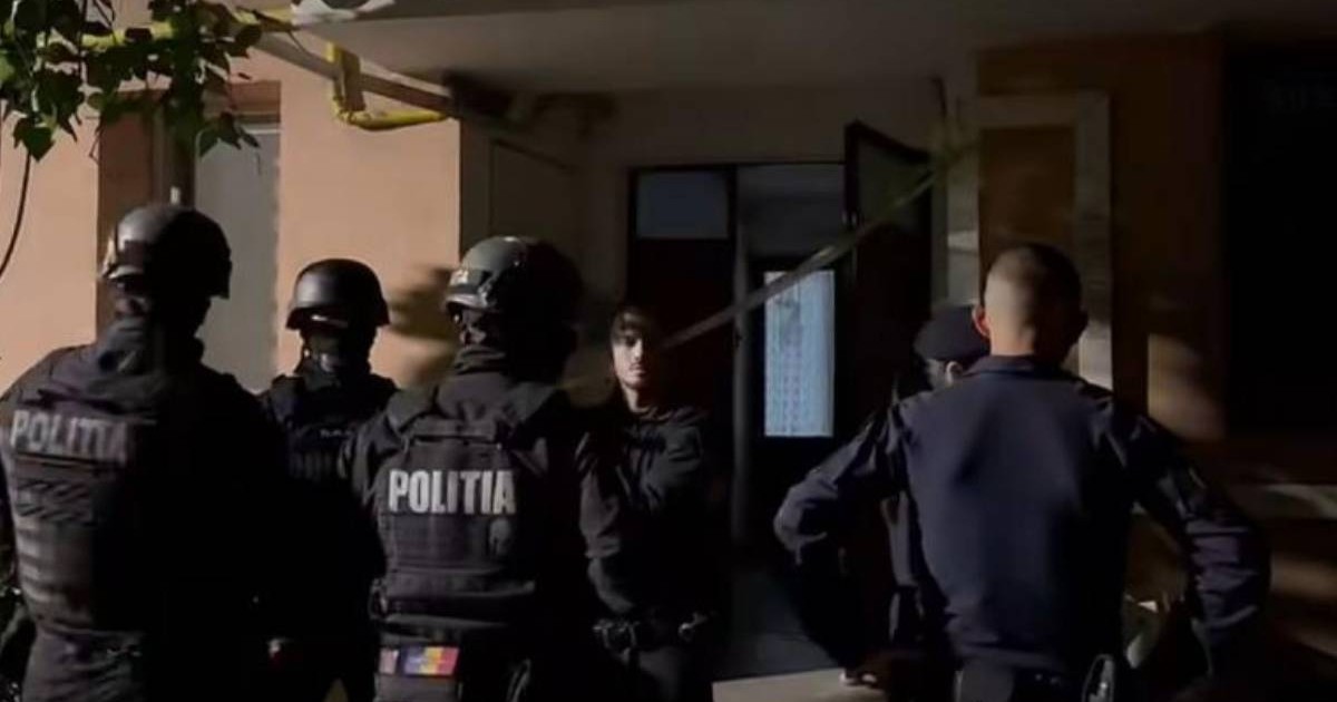 Mai mulți polițiști și luptători ai trupelor speciale stau în fața intrării unui bloc, noaptea, în timpul intervenției din cazul crimei din Târgu Jiu.