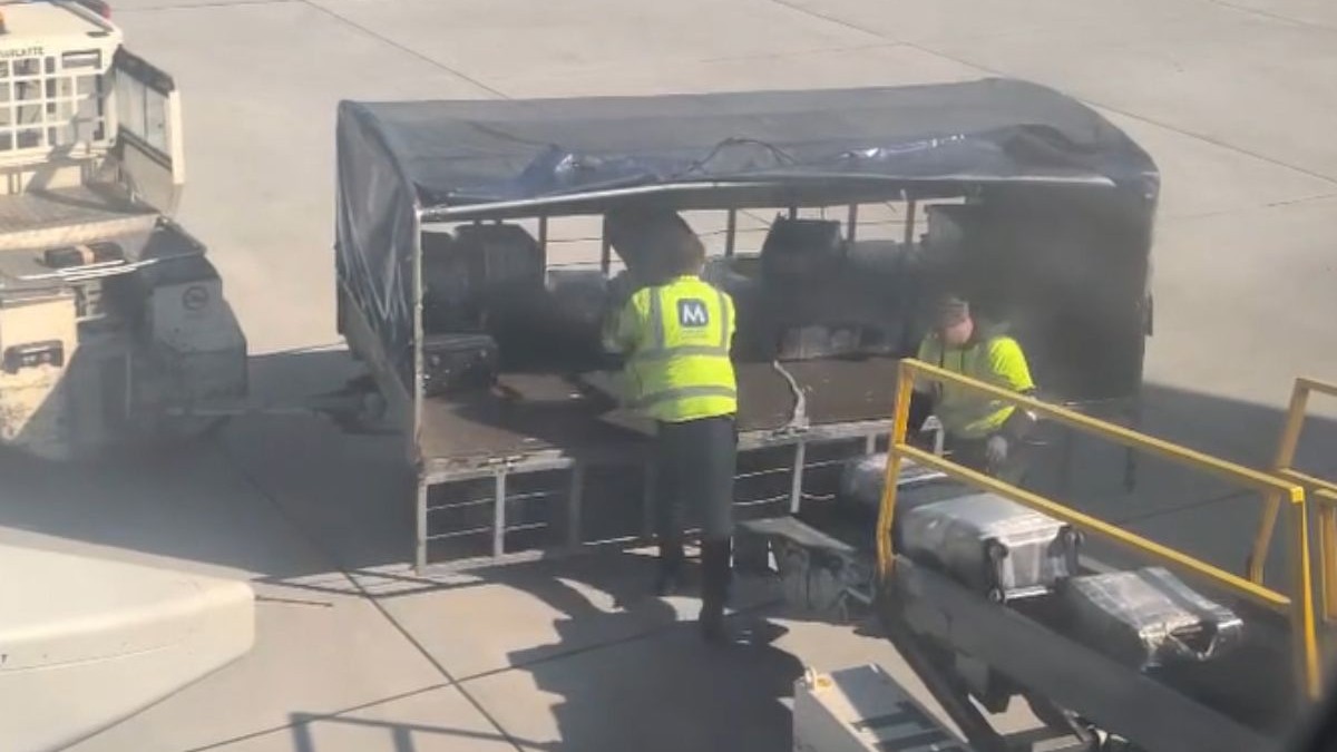 doi angajați ai aeroportului internațional cluj napoca, îmbrăcați în jachete verzi fosforescente cu litera M pe spate, scrisă cu albastru, aranjează trolere într-un vehicul de transport