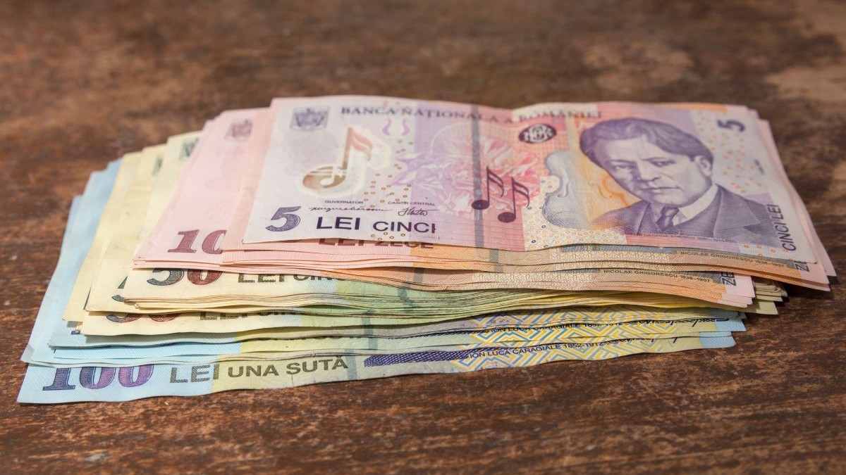Bani pe o masă, mai multe bancnote de 5, 50 și 100 de lei pe o masă de culoare maro