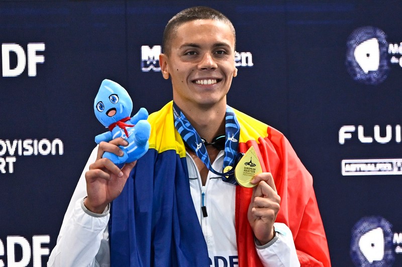 David Popovici ține steagul tricolor pe podiumul de premiere, după ce a cucerit aurul în proba de 100 metri la Campionatul european de laParis, 12 august 2026