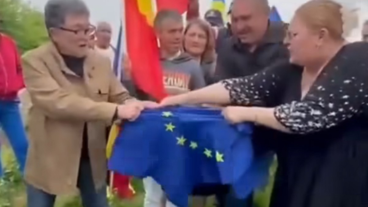 Imaginea o surprinde pe Diana Șoșoacă în timp ce rupe un steag al Uniunii Europene alături de un bărbat, în fața unui grup de oameni și a mai multor steaguri ale României. Scena pare să aibă loc în aer liber, în timpul unui moment transmis public și intens comentat pe rețelele sociale.