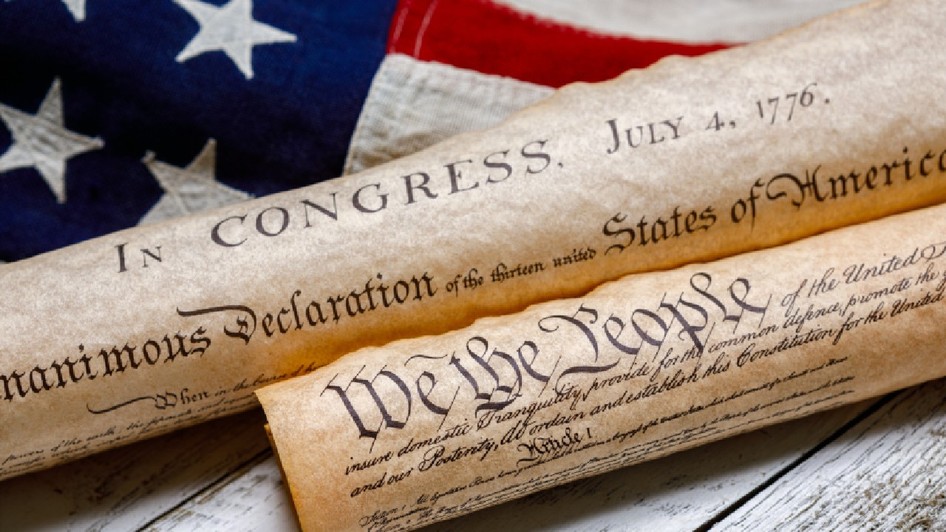 Exemplare înfășurate ale Constituției SUA și ale Declarației de Independență, alături de un steag american de epocă, pe lemn vopsit în alb și cu aspect patinat