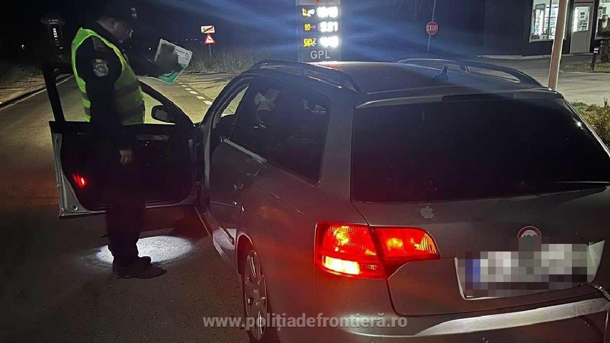 Un polițist de frontieră verifică actele unui șofer, noaptea, usa soferului este deschisă