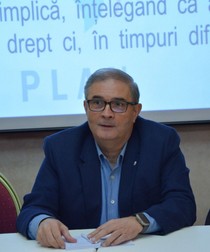 Un barbat in sacou albastru stă la o masă