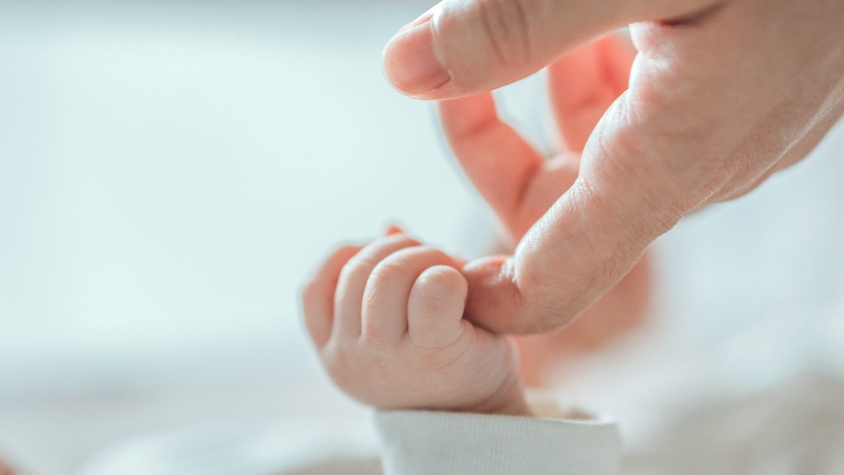 O persoană care ține cu degetul mâna unui bebeluș.