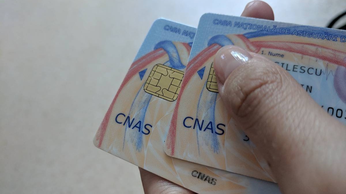 O persoană care ține două carduri de sănătate în mână