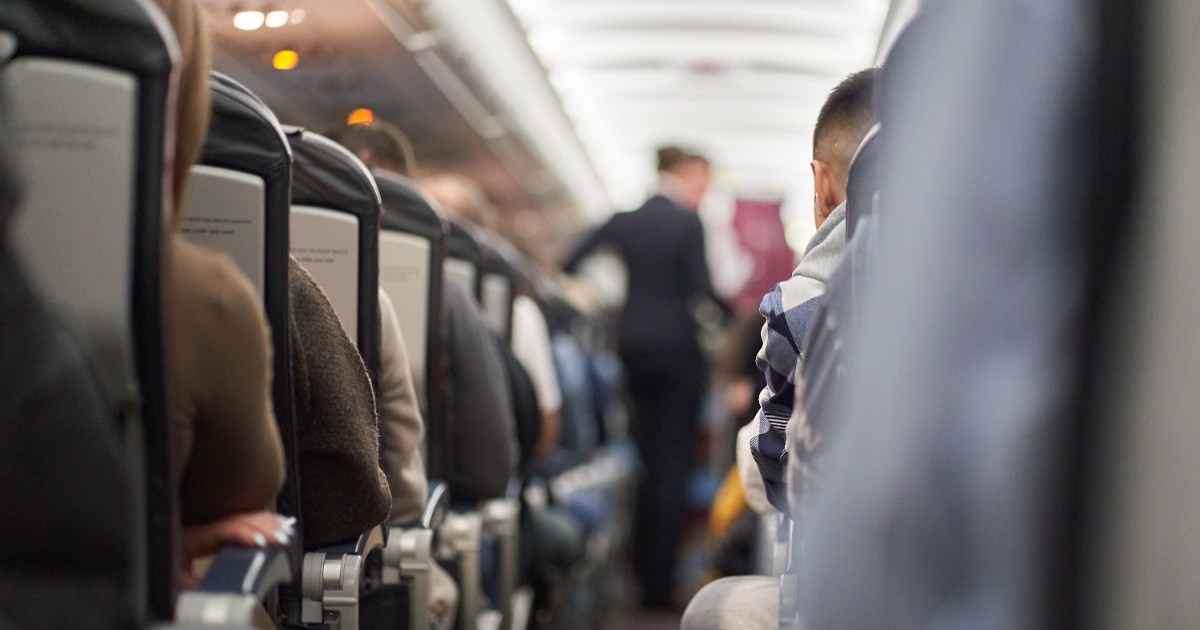 Pasageri la bordul unui avion, oamenii stau așezați pe scaune, o femeie se plină pe culoar