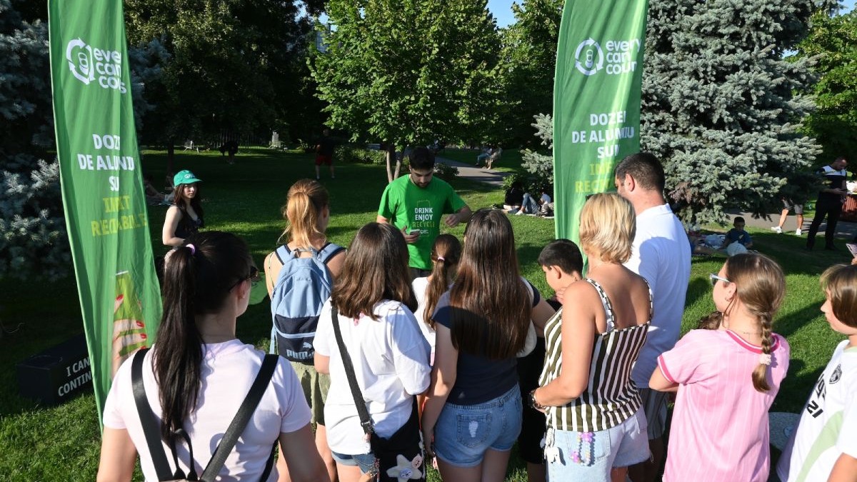 Tineri într-un parc, pe timp de vară, cu două bannere de culoare verde și vegetați verde pe fundal