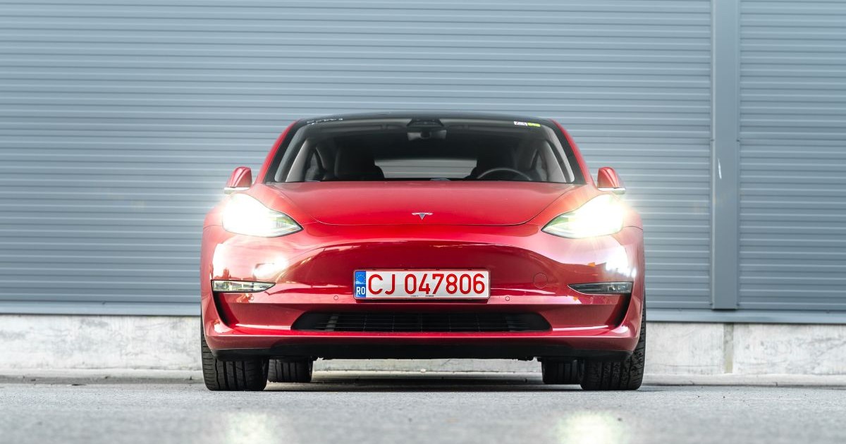 Tesla Model 3, de culoare roși, din față, cu farurile aprinse, cu numere provizorii de Cluj