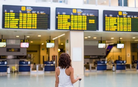O femeie care se uită la panourile cu informații despre zboruri din aeroport