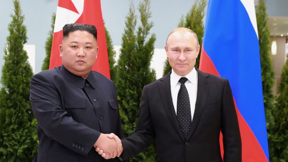 In imagine Kim Jong-un, liderul Nord coreean, imveacat complet in negru, dă mâna cu Vladimir Putin, in constum negru si cămasă albă, in spatele lor sunt steagurile celor doua tari