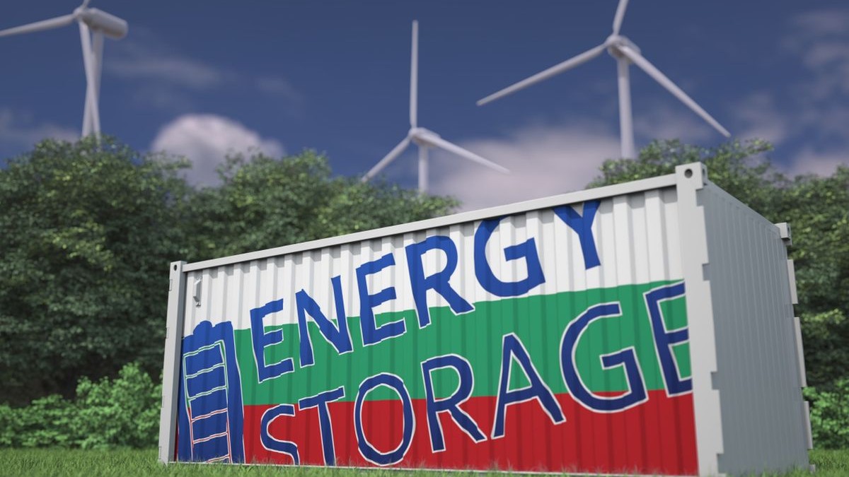 O baterie de stocare a energiei cu steagul Bulgariei suprapus, iar pe baterie scrie Energy Storage, iar în spate se văd turbine eoliene
