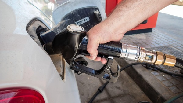 O mână care ține pistolul unei pompe de carburant introdus în rezervorul unui autoturism alb etichetat „DIESEL” într-o stație de alimentare.