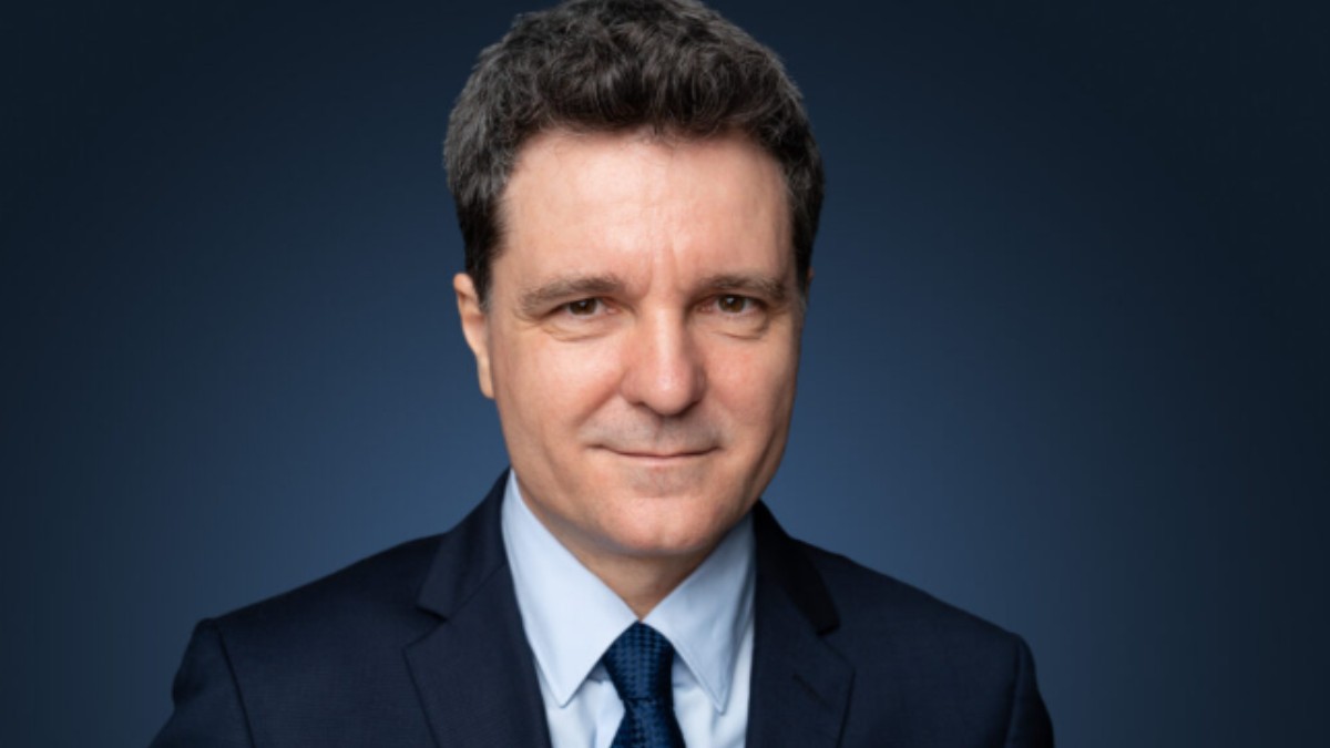 În imagine este ilustrat Nicușor Dan, îmbrăcat în costum albastru închis, cămașă și cravată albastră.