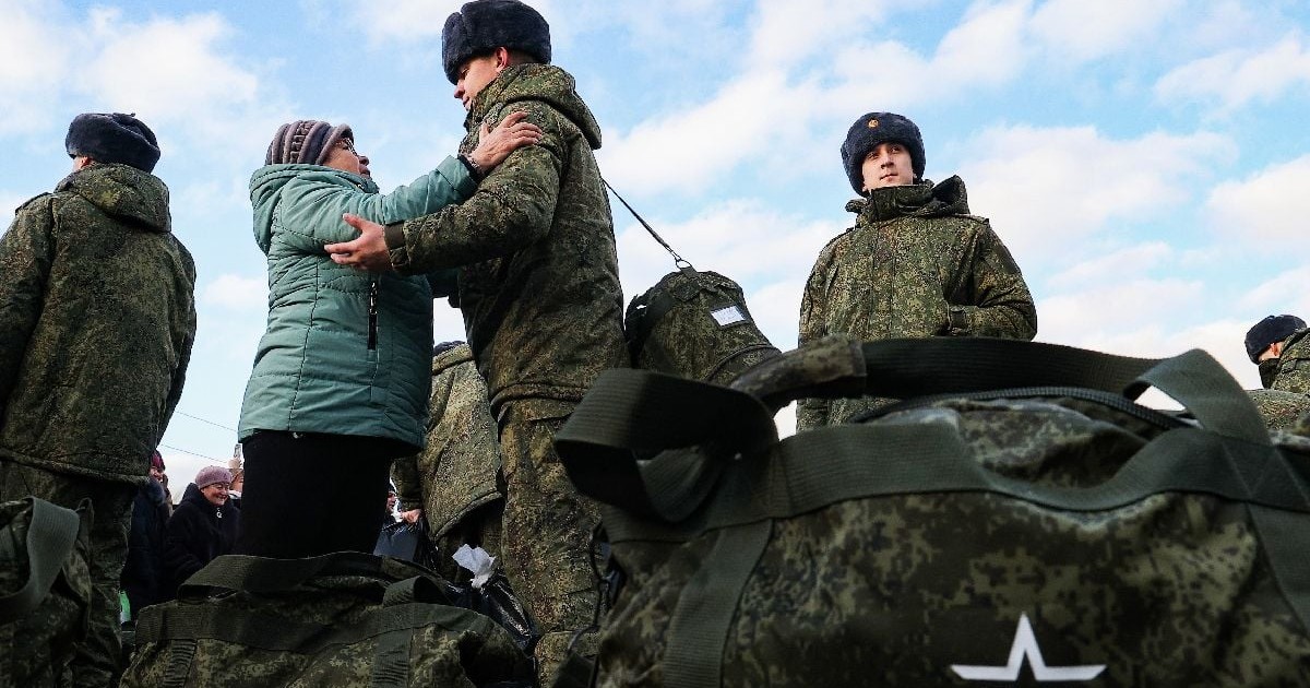 Soldați tineri lângă genți militare, unul dintre ei îmbrățișează o femeie în vârstă
