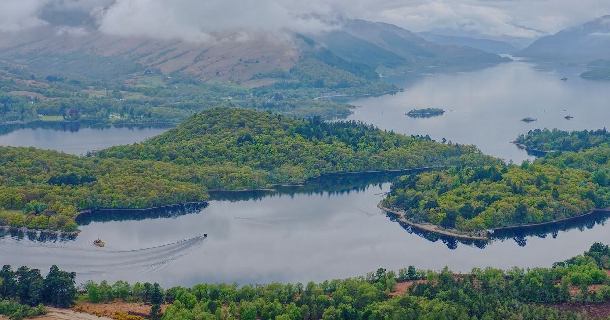 O vedere aeriană surprinde un lac înconjurat de insule împădurite și dealuri acoperite de ceață.