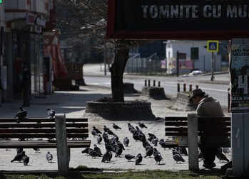 Un bătrân hrănește porumbeii pe o bancă de lângă Gara din Predeal
