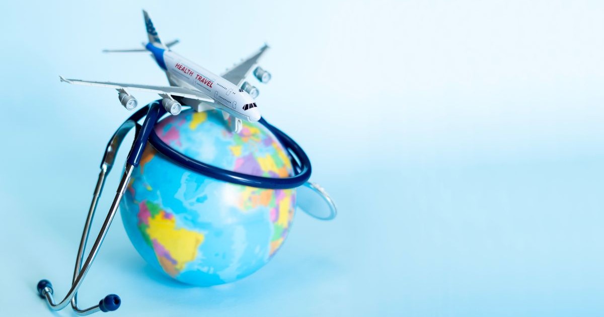 glob pământesc în miniatură, pe care este așezat un model de avion de jucărie având inscripționat pe fuzelaj un text legat de călătorii medicale. În jurul globului este înfășurat un stetoscop medical, cu tuburile și componentele sale metalice poziționate în preajmă, întregul ansamblu fiind plasat pe o suprafață uniformă, lăsând o zonă liberă în partea dreaptă a compoziției.