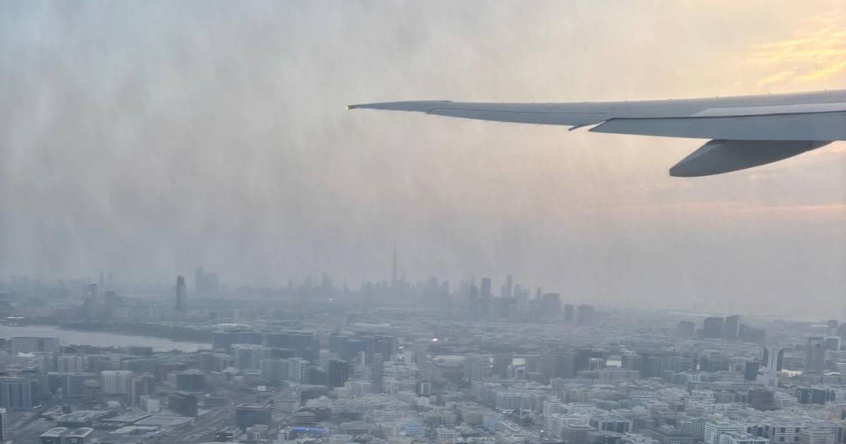 Vedere aeriană asupra orașului Dubai dintr-un avion, cu aripa aeronavei și zgârie-norii orașului în depărtare. Cerul este cenușiu de praf și fum Foto: Alex Donovici / Facebook