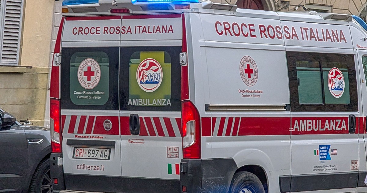 Imaginea surprinde partea din spate a unei ambulanțe aparținând Crucii Roșii Italiene (Croce Rossa Italiana), pe o stradă, cu girofarurile albastre aprinse.